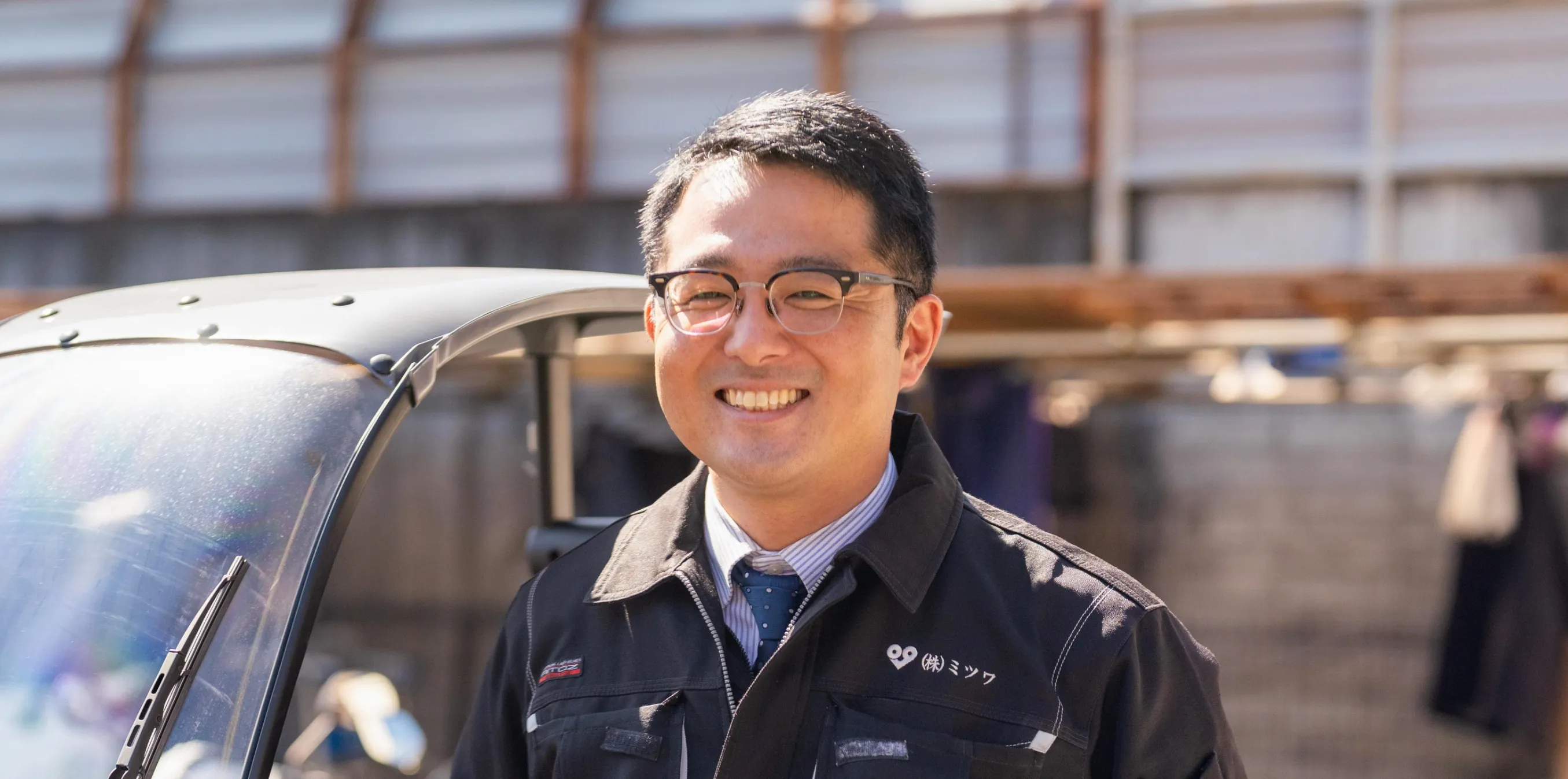 車の隣で笑顔で正面を見ているスタッフ